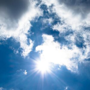 A vivid view of the sun shining through fluffy clouds in a bright blue sky.